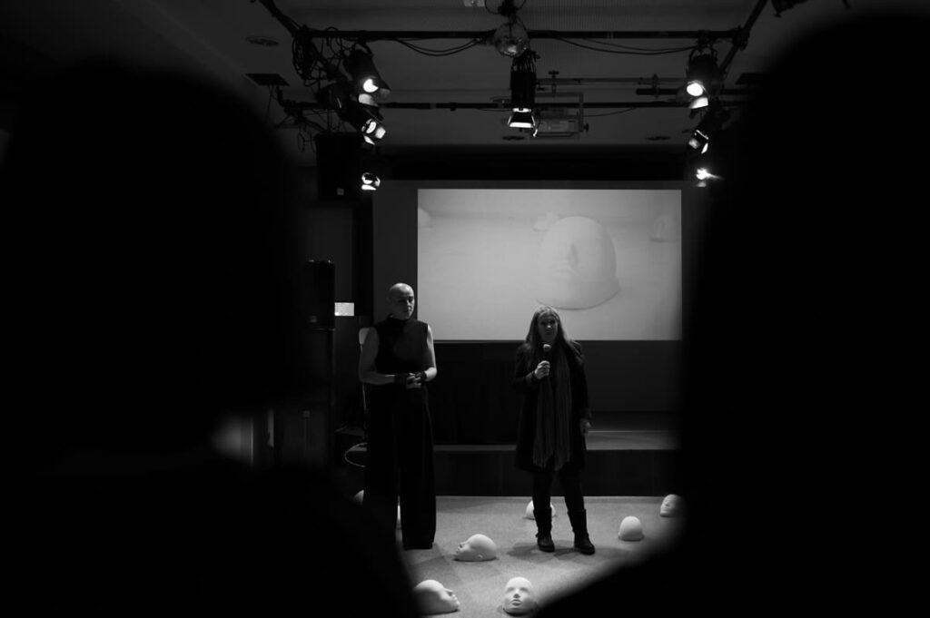 Two people standing in front of crowd surrounded by sculptures